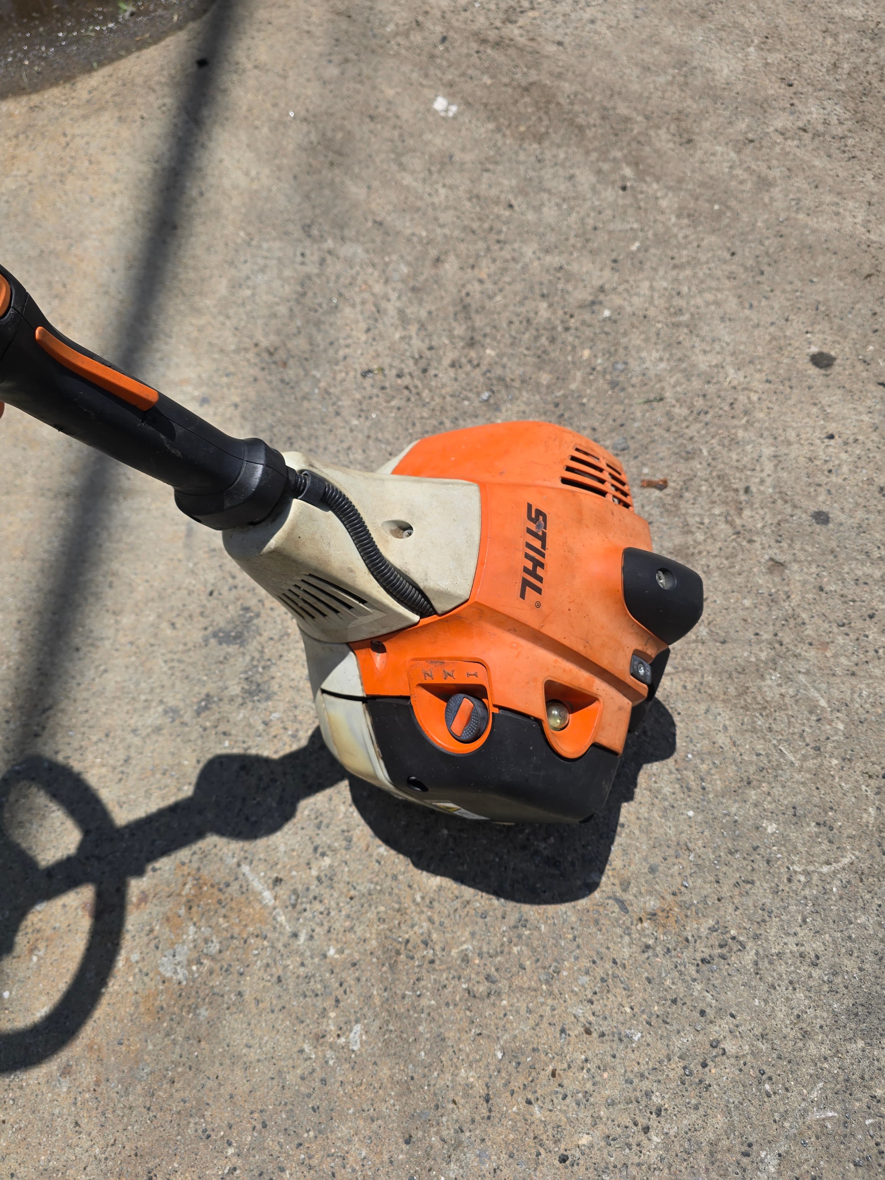 Orange and white Stihl string trimmer engine resting on a gray concrete surface.