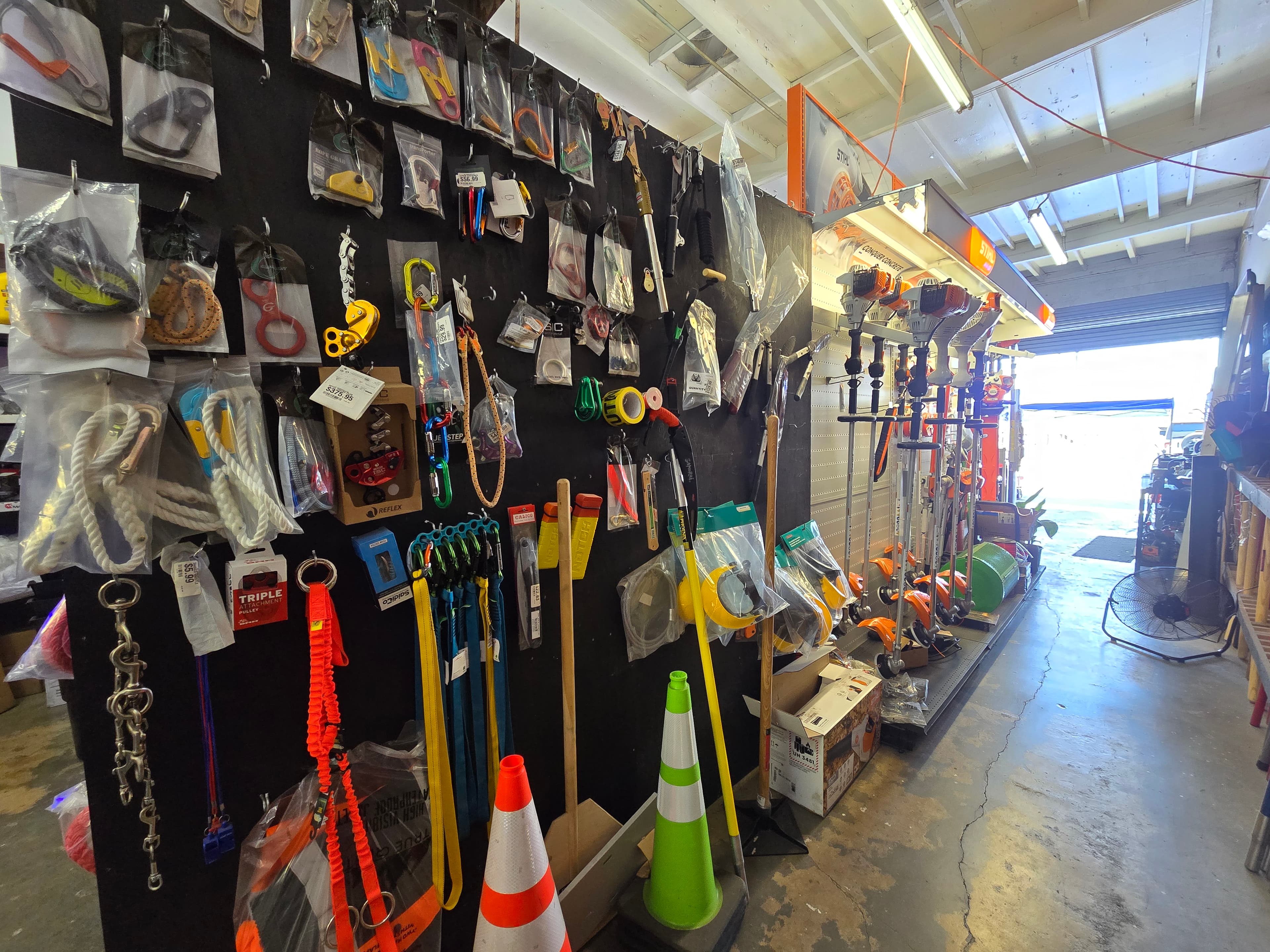 Climbing ropes, carabiners, and safety gear displayed on a black wall in a hardware shop.